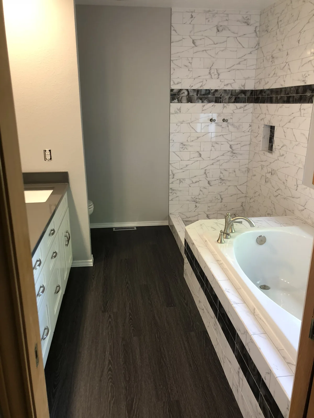 Bathroom with a marble-tiled drop-in tub and white vanity on dark wood flooring