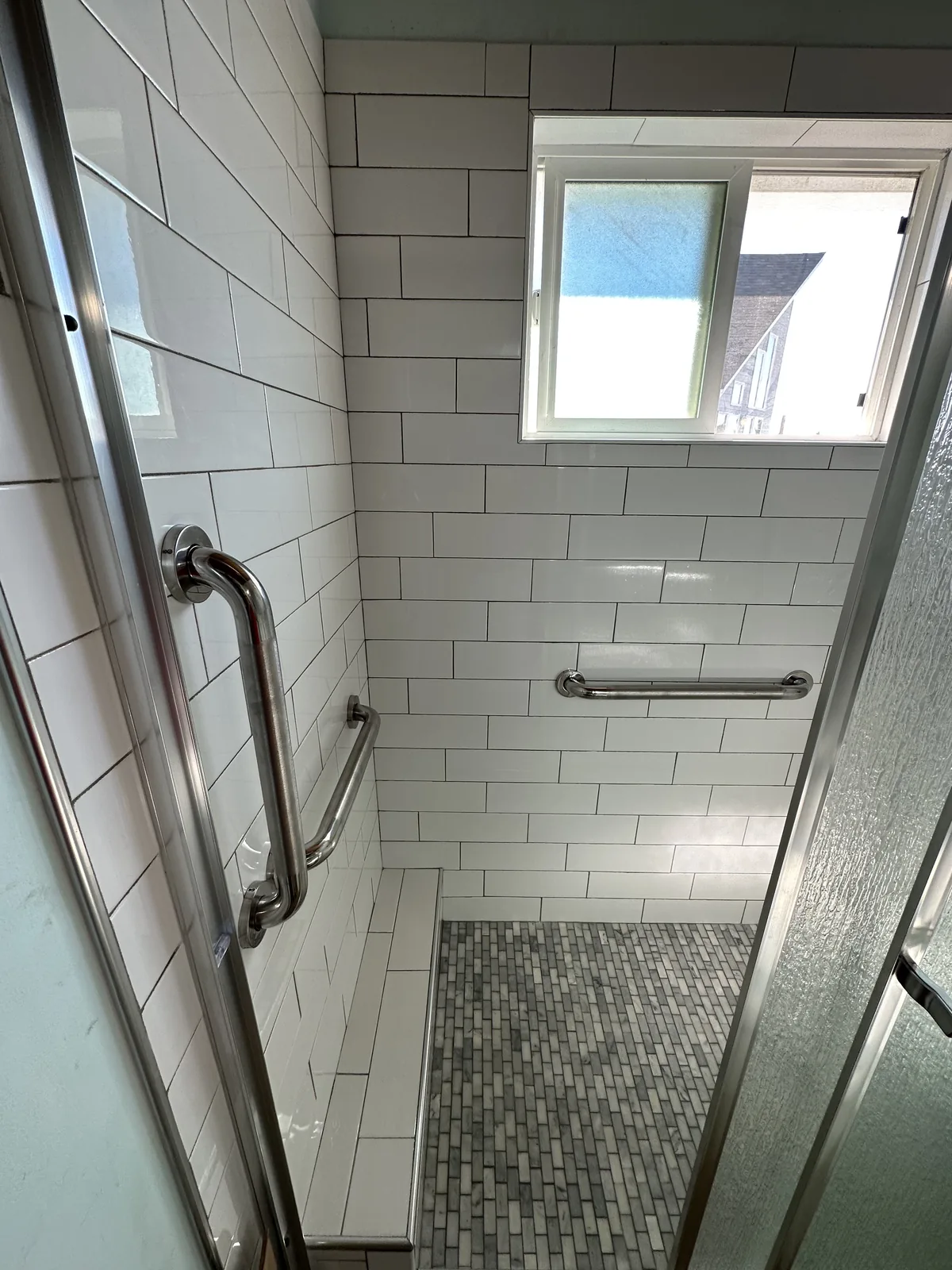 Accessible walk-in shower with white subway tile, grab bars and a marble mosaic floor