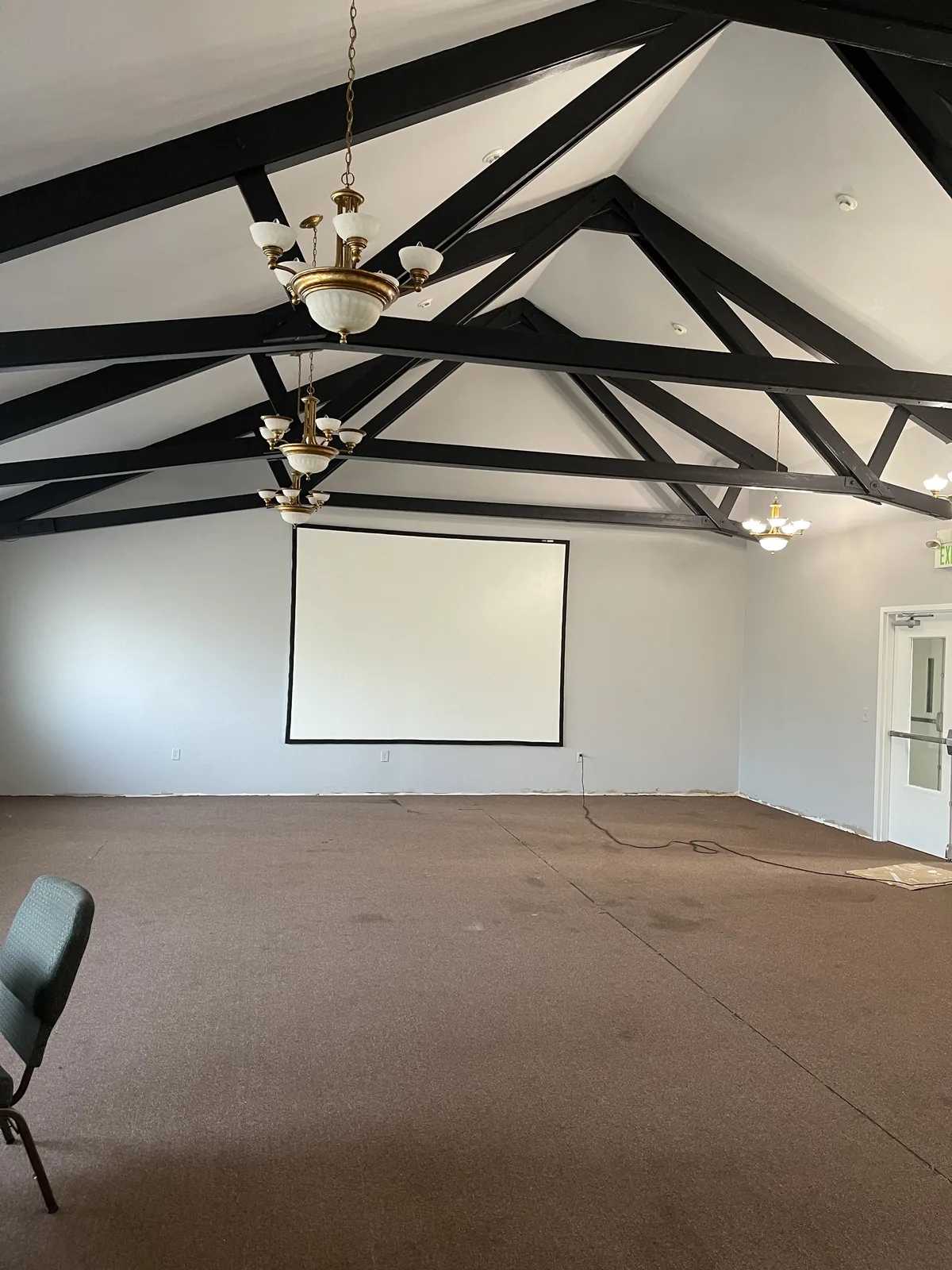 Church hall with black-painted roof trusses and grey walls during a repaint