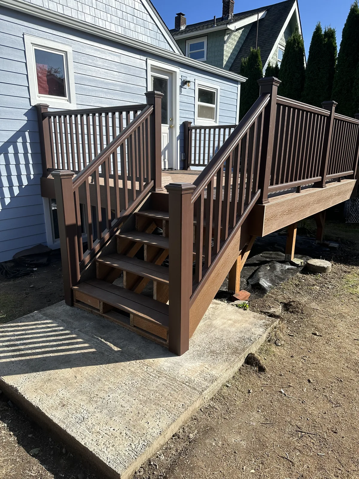 Brown composite deck with matching railings and stairs beside a blue house