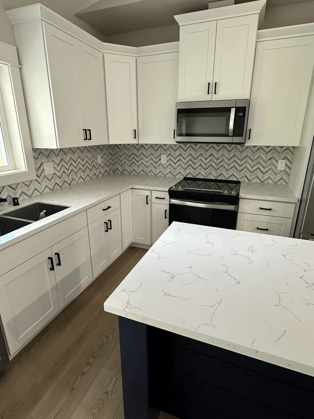 Remodeled kitchen with white shaker cabinets, quartz counters and a navy island