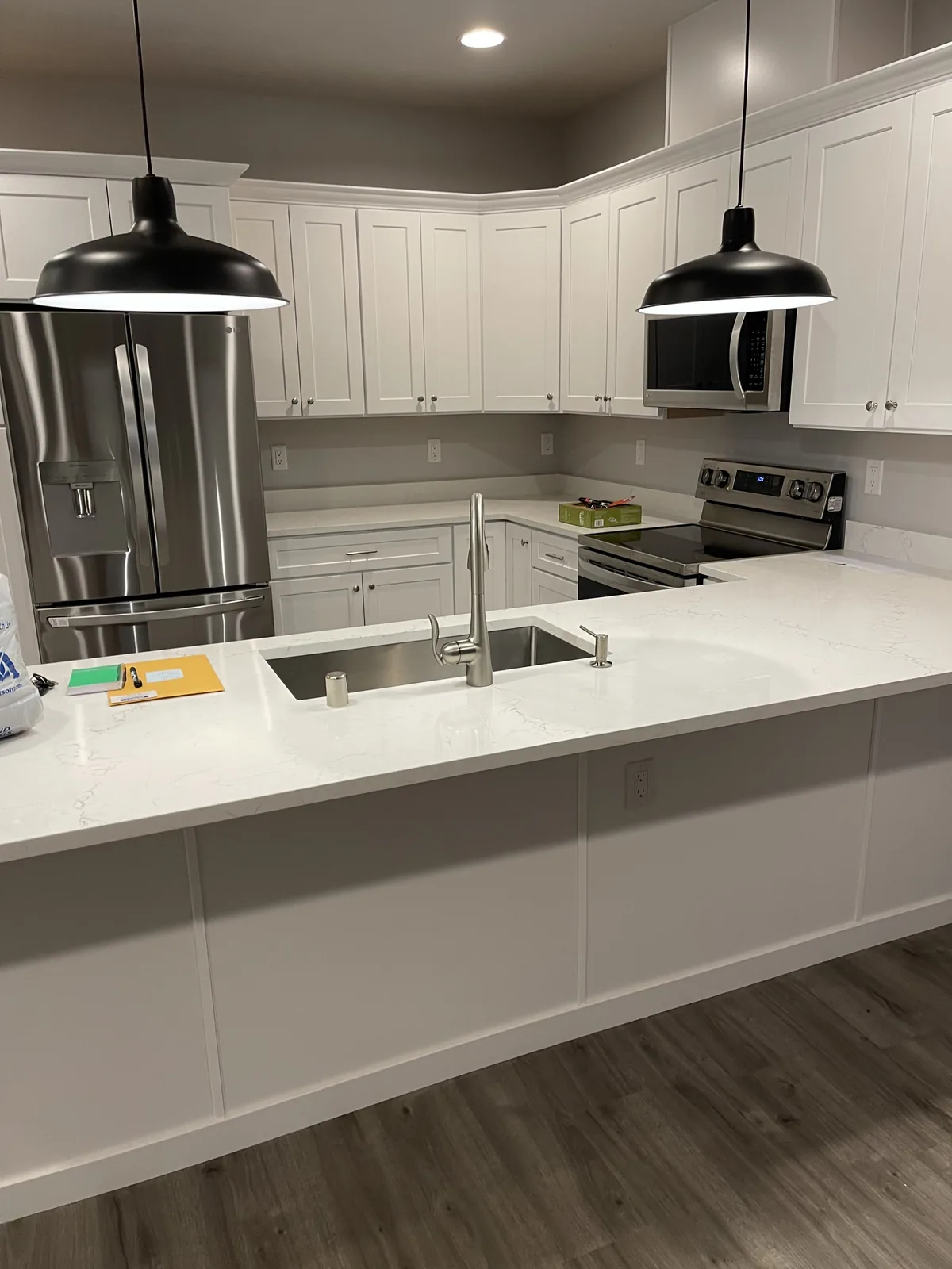 White kitchen with black pendant lights, a quartz peninsula and stainless appliances