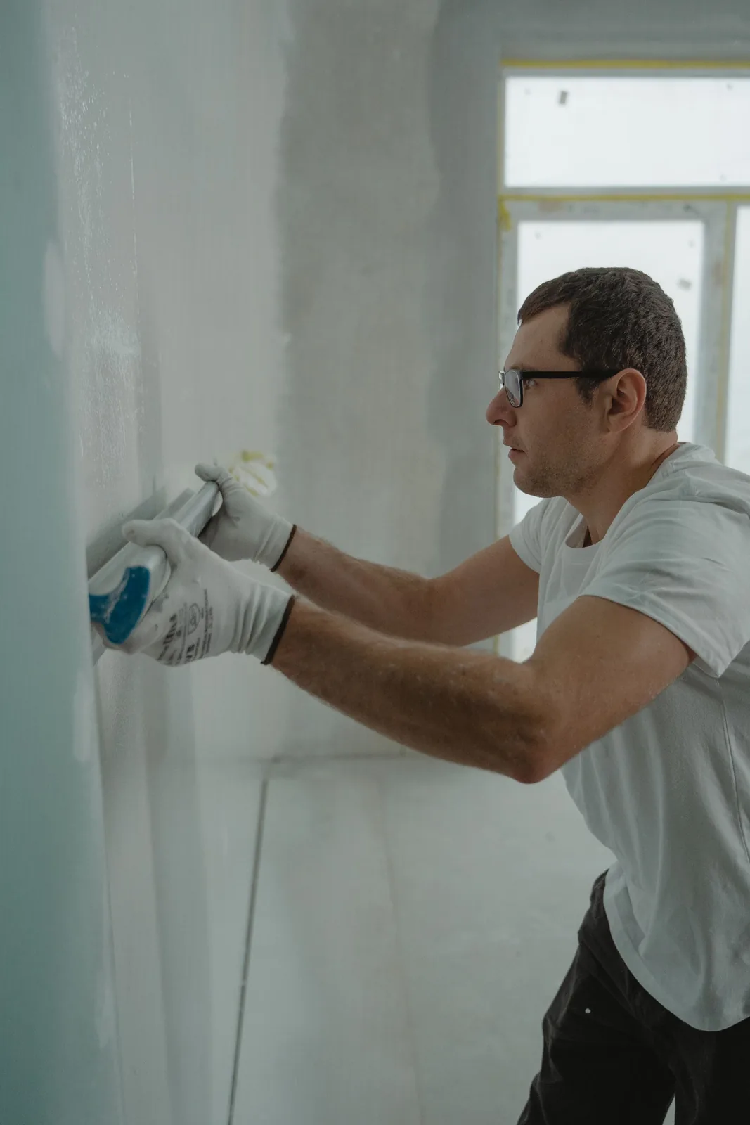 Worker smoothing drywall compound over a seam during a home renovation
